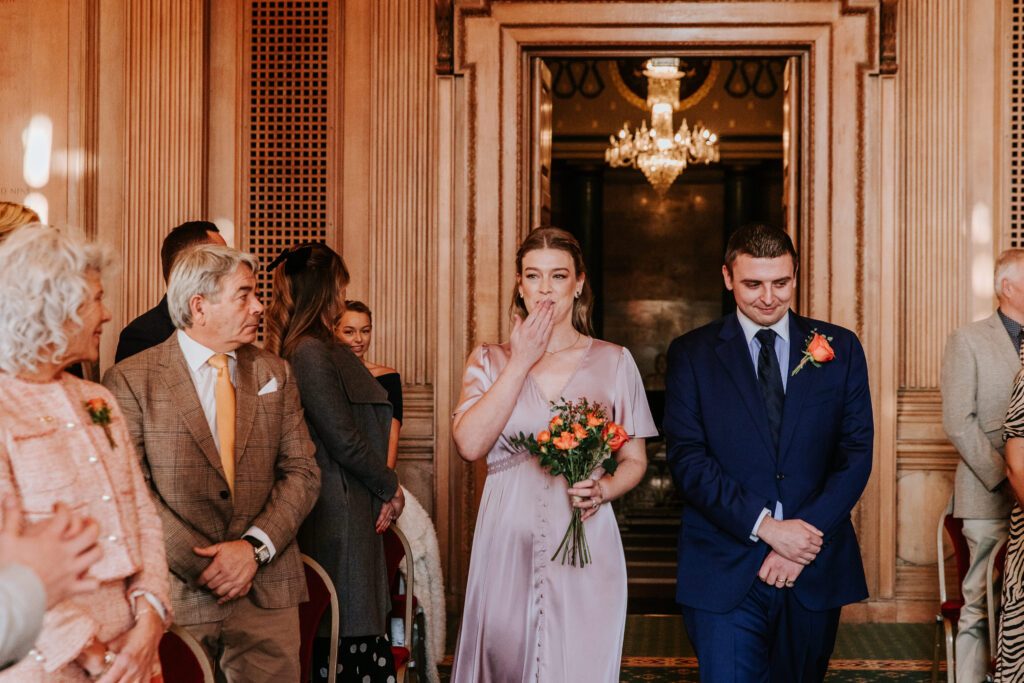 Two people walking down aisle as part of procession at a wedding